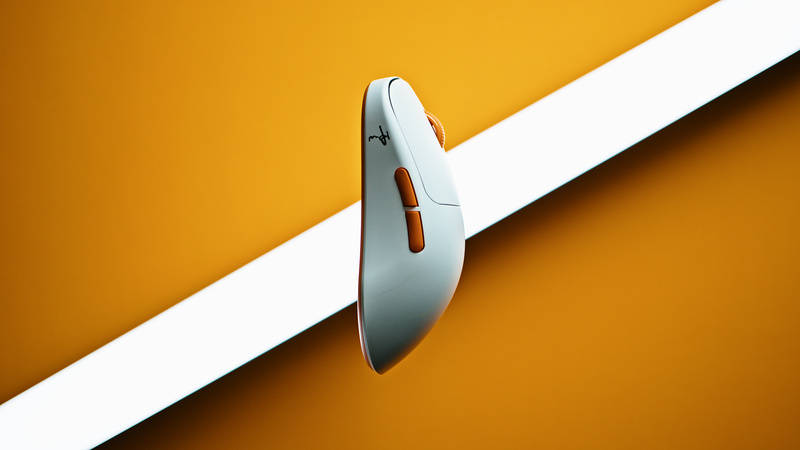 White gaming mouse with orange side buttons on an orange background crossed by a white light strip