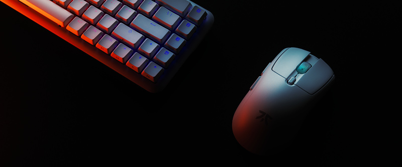 Compact keyboard and white gaming mouse on black, lit warm from one side and cool from the other