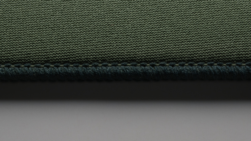 Macro of a dark green knit mousepad surface and stitched edge falling off into soft focus